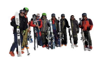 Gruppe von Skifahrern mit Helmen und Skiern steht auf schneebedecktem Berg.