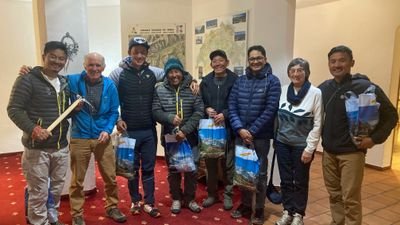 Eine Gruppe von acht Personen in Freizeitkleidung steht in einem Innenraum mit Karten an der Wand.