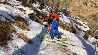 Person mit Skiern und Rucksack auf schneebedecktem Hang in bergiger Landschaft.
