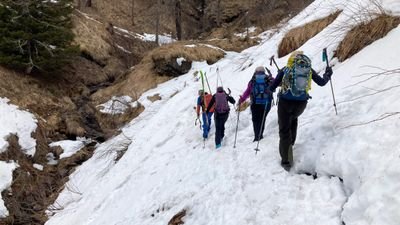 Personen mit Rucksäcken und Stöcken wandern auf schneebedecktem Bergpfad.