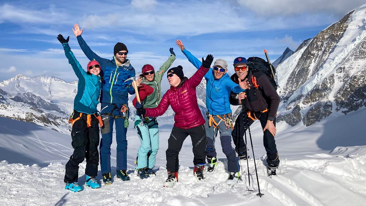 Group of people with climbing gear and ski poles on a snow-covered mountain peak.