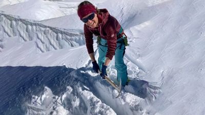 Person with ice axe and climbing harness on snow-covered mountain peak.