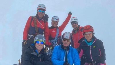 Group of six people with helmets and climbing equipment in a foggy mountain landscape.