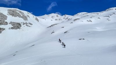 Group of people with skis and poles on a snowy mountain under a blue sky.