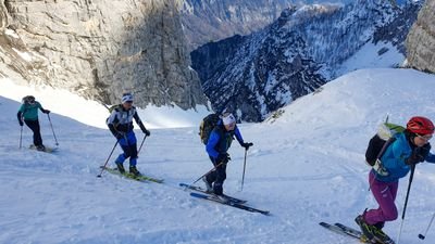 Four people with skis and helmets are climbing a snowy mountain.