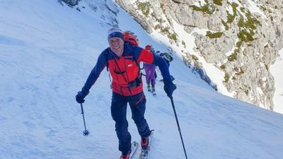 People with skis and poles are climbing a snowy mountain. They are wearing winter clothing.
