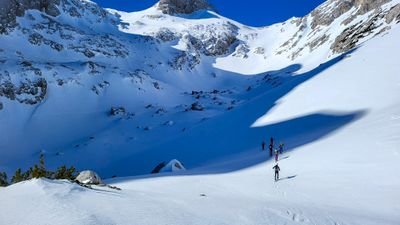 People ski touring in snow-covered mountains, carrying skis and poles.