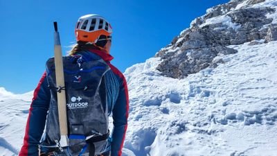 Person with helmet and backpack is climbing in the snow in the mountains. Ice pick attached to the backpack.