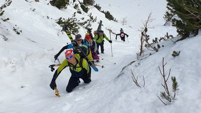 Group of ski tourers with helmets and skis climbing a snow-covered slope in the mountains.