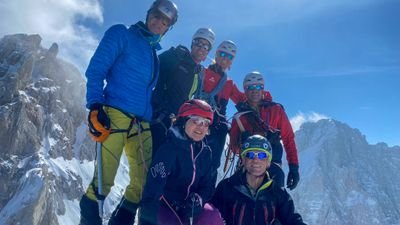 Six people with helmets and climbing equipment on a snow-covered mountain peak.