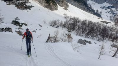 Person ski touring with poles and backpack in a snow-covered mountain landscape.