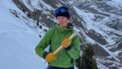 Eine Person in Winterkleidung mit Eispickel in verschneiter Berglandschaft.