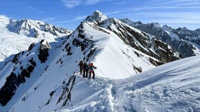 Drei Personen mit Helmen und Kletterausrüstung auf einem schneebedeckten Berggrat in den Alpen.