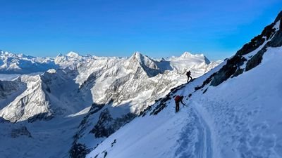 Bergsteiger mit Helmen und Kletterausrüstung auf schneebedecktem Bergpfad in den Alpen.