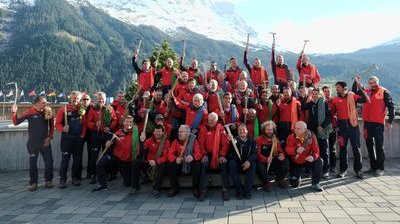 Group of people in red jackets with ice axes in front of a mountain backdrop.