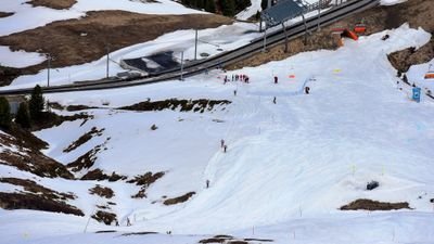 Skifahrer auf schneebedeckter Piste in den Bergen, mit Helmen und Skiausrüstung, nahe einer Straße.
