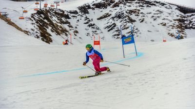 Skier with helmet and ski poles on a snow-covered slope in the mountains, passing through a slalom gate.