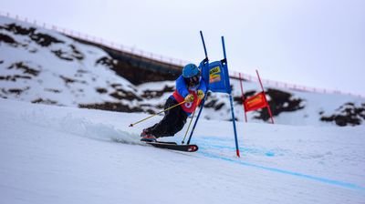 Skifahrer mit Helm und Skistöcken fährt Slalom auf schneebedecktem Berg.