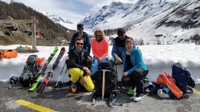A group of people with ski equipment is sitting on a road in a snowy mountain landscape.