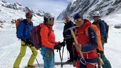 Five people with helmets and skis in snowy mountains, one person is holding an ice pick.