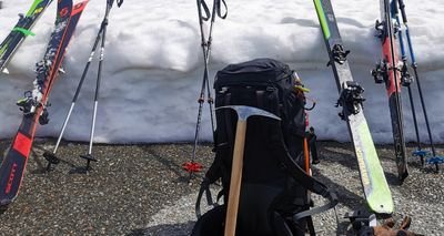 Ski equipment with skis, poles, backpack, and ice pick placed in front of a snow wall.