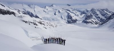 Gruppe von Skifahrern mit Stöcken auf verschneitem Berggipfel, umgeben von Alpenpanorama.