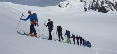 Personengruppe beim Skitourengehen in verschneiten Bergen, mit Skistöcken und Rucksäcken.