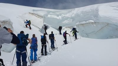 Gruppe von Menschen mit Wanderstöcken und Rucksäcken auf einem verschneiten Gletscher.