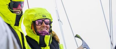 People in yellow jackets and sunglasses on a sailboat, holding a sail tool.
