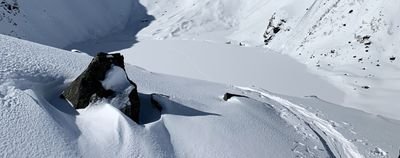 Snow-covered mountain landscape with rocks and ski tracks, surrounded by snow-covered slopes.