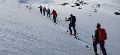 Group of people with skis and backpacks ascending a snow-covered mountain.
