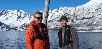 Two people with life jackets on a boat in front of snow-covered mountains and a lake.