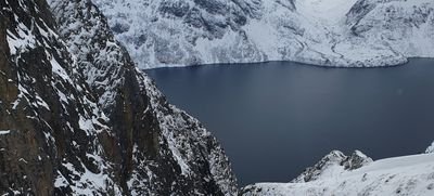 Snow-covered mountain landscape with a view of a lake, surrounded by rugged cliffs.