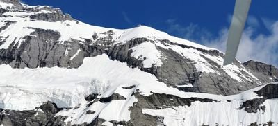 Verschneite Berglandschaft mit Felswänden und Gletscher unter blauem Himmel.