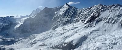 Snow-covered mountain landscape in the Alps with steep peaks and clear sky in the background.