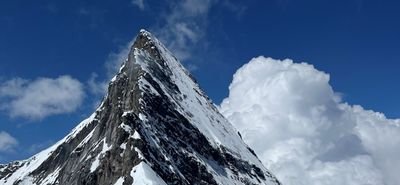 Snow-covered mountain peak under a blue sky with clouds in the background.