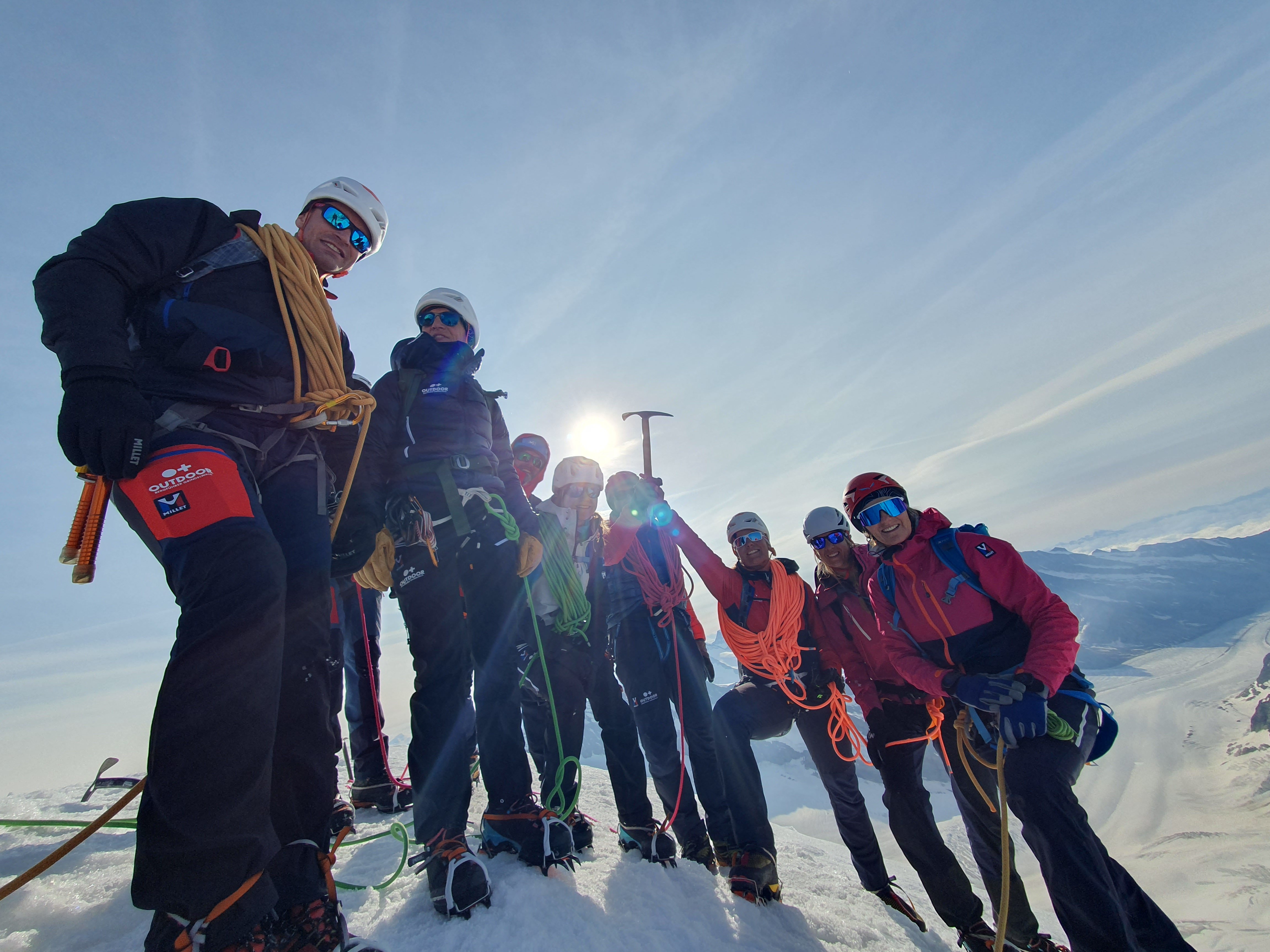 Group of mountaineers with helmets and ropes on a snow-covered summit in the mountains.