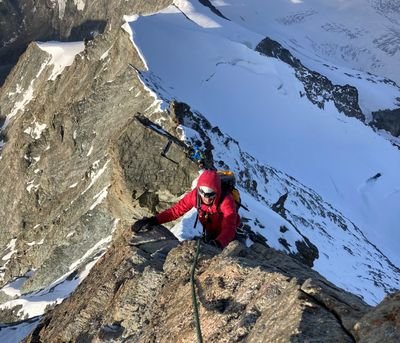 Kletterer mit Helm und Seil auf schneebedecktem Berggrat in den Alpen.