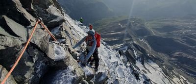 People with helmets and climbing gear are climbing up a secured mountain path; snowy alpine landscape.