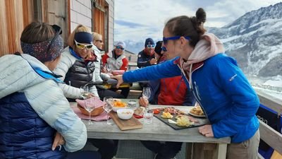 Frau serviert einer Gruppe in der Konkordiahütte einen Aperitif.