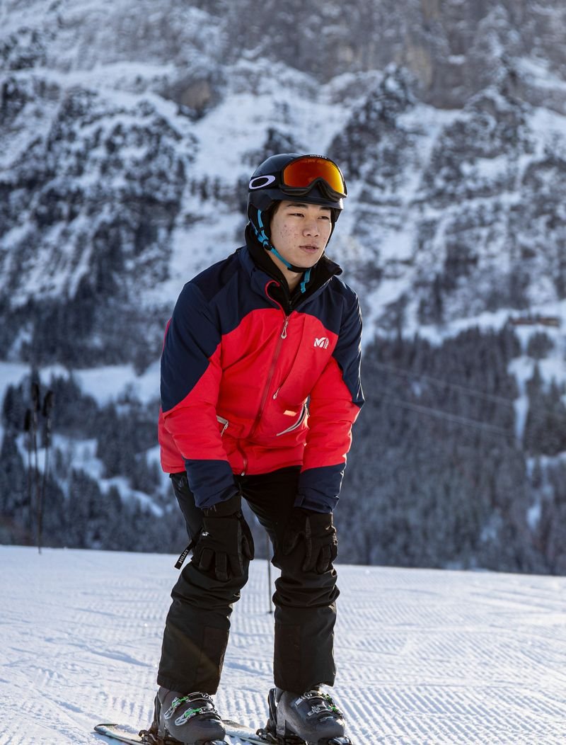 Person on skis with helmet and ski goggles on snowy mountain in front of rocky scenery.