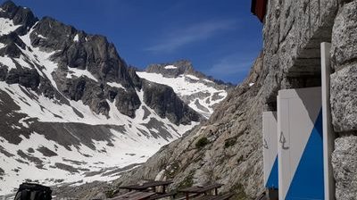 Snow-covered mountains with rocky peaks, adjacent to a stone building and picnic tables.