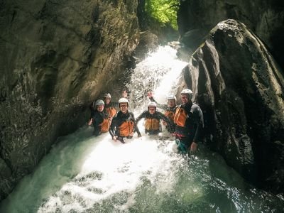 Eine Gruppe von Canyoning-Teilnehmern steht vor einem Wasserfall in einer engen Felsschlucht.