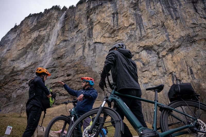 People with helmets and bicycles in front of a steep rock face.