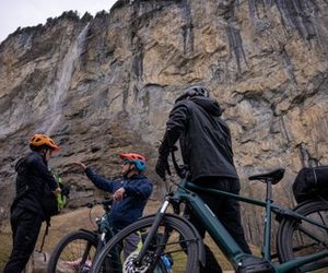 People with helmets and bicycles in front of a steep rock face.