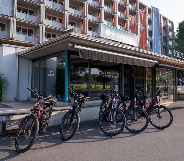 Bicycles parked outside an adventure company building with signage and a multi-story structure behind.