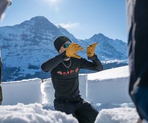 Person in winter clothing with gloves in the snow, surrounded by mountains, building snow blocks.