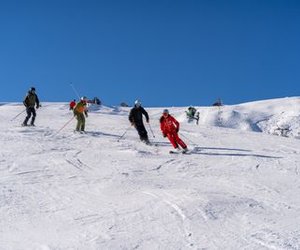 Several people are skiing with helmets on a snow-covered slope in the mountains.