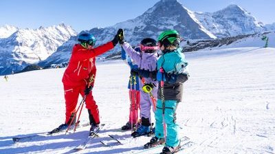 Personen mit Skiausrüstung und Helmen auf verschneitem Berg, geben sich High-Five.