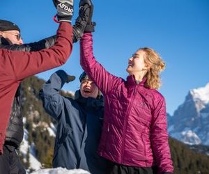 People in winter clothing are giving each other high-fives in a snowy mountain landscape.